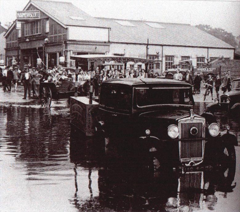 Photograph. Peruzzis' ice cream cart being towed through floods under the M&GN Railway Bridge. Harmer & Scott's Garage in background (North Walsham Archive).